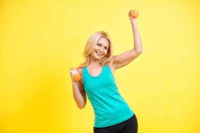 Young woman exercising against yellow background