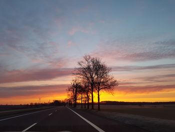 Road by trees against sky during sunset