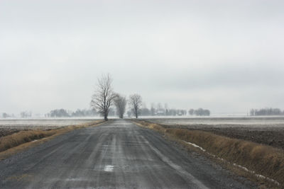 Road amidst field against sky during winter