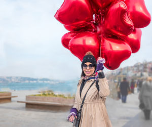 Portrait of woman holding balloons against sky