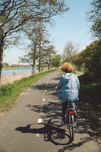 Rear view of woman riding bicycle on road during sunny day