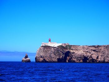 Lighthouse by sea against clear blue sky