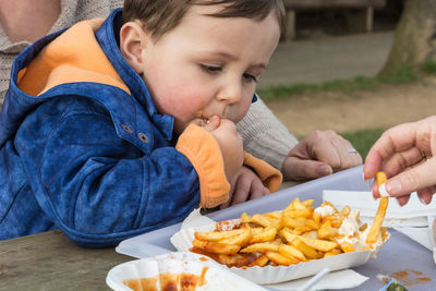 Close-up of boy eating french fries while sitting with mother at table