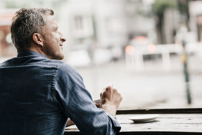 Rear view of man looking away while sitting on table in city