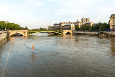 Notre dame de paris by bridge and river against sky in city