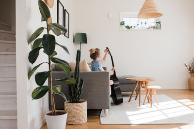 Young girl tuning her guitar whilst sat on the couch at home