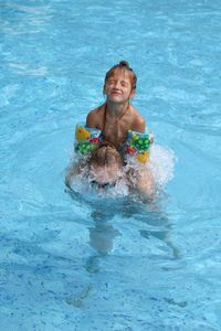 Mother giving piggyback to daughter in swimming pool