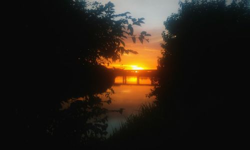 Silhouette trees by lake against sky during sunset