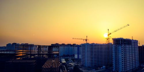 Cranes in city against sky during sunset
