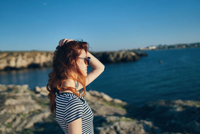 Woman standing by sea against blue sky