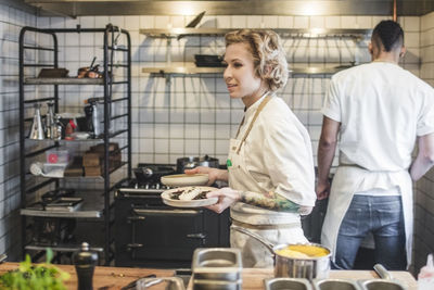 Side view of confident waitress carrying food plates in kitchen at restaurant