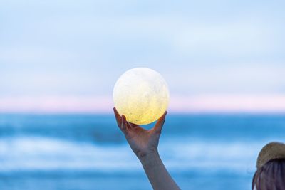 Person holding crystal ball at beach against sky during sunset