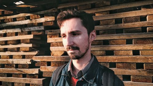 Close-up of thoughtful young man standing against stacked planks