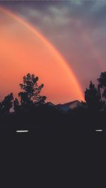 Silhouette trees against rainbow in sky at sunset