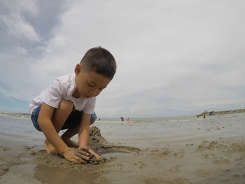 Full length of boy playing on beach against sky