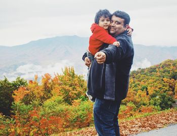 Portrait of man carrying son on road against mountains