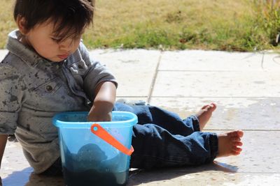 Boy with bucket sitting on footpath