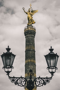 Low angle view of monument and lamp post against cloudy sky