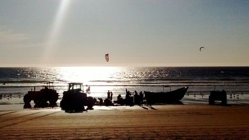 Silhouette people on beach against sky during sunset