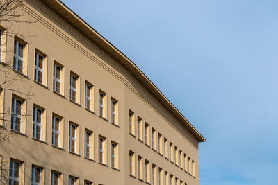 Corner of a building against blue sky. beige plaster, simple, linear cornice and row of windows. 