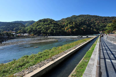 Scenic view of river by mountains against clear blue sky