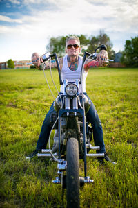 Man sitting on motorcycle at grassy field against sky