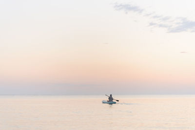 Boy with oar paddleboarding on sea during sunset