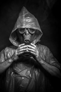 Man in raincoat wearing gas mask against black background