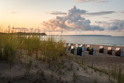 Hooded chairs on beach against sky during sunset