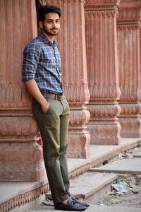 Young man looking away while standing by column