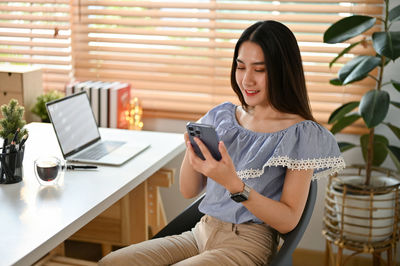 Young woman using mobile phone while sitting at home