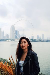 Fashionable young woman standing against sea and urban skyline