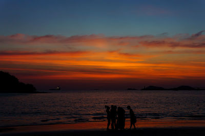 Silhouette people on beach against sky during sunset