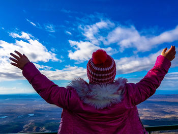 Rear view of girl with arms raised standing on observation point against blue sky