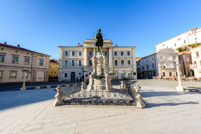 Fountain in city against clear blue sky