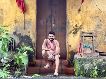 Portrait of young man sitting against wall