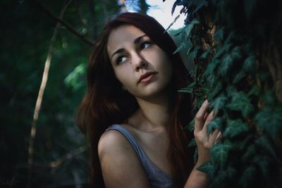 Thoughtful young woman leaning on tree in forest