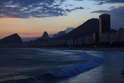 Silhouette buildings by sea against sky during sunset