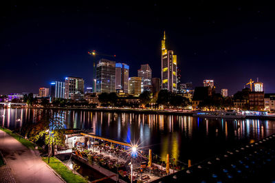 Illuminated buildings by river against sky at night