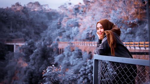 Smiling woman looking away while standing by railing during winter