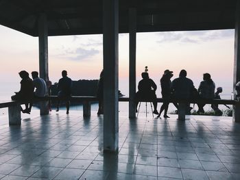 Silhouette people sitting on tiled floor against sky