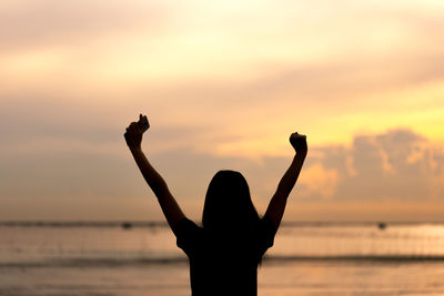 Silhouette woman standing at beach against sky during sunset