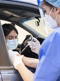 Woman getting coronavirus vaccine from female frontline worker in car