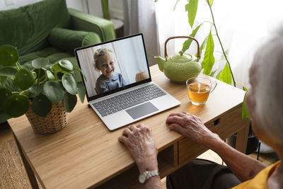 Senior woman talking on video call with granddaughter through laptop