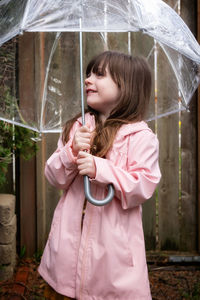 Cute girl holding umbrella while standing during rain