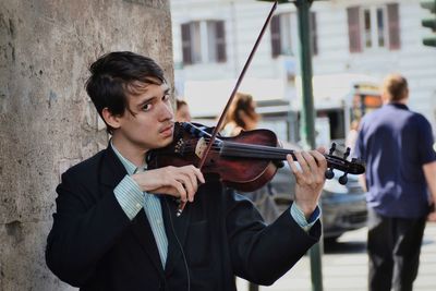 Portrait of street musician playing violin against wall