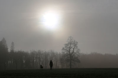 Silhouette of woman with dog on field against sky