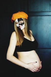 Pregnant woman with painted face standing at home during halloween