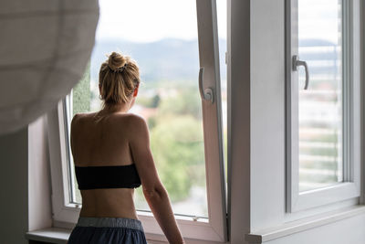 Rear view of woman looking through window at home