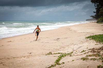 Rear view of woman walking at beach against sky
